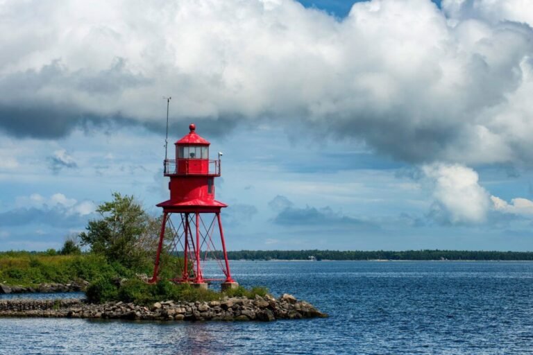 Small red lighthouse with skeleton scaffolding overlooking water.