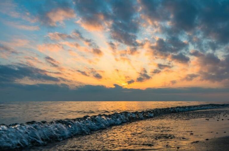 Waves crashing on a beach at sunset.