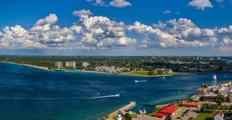 Boats sailing into a bay with buildings and trees along the shore.