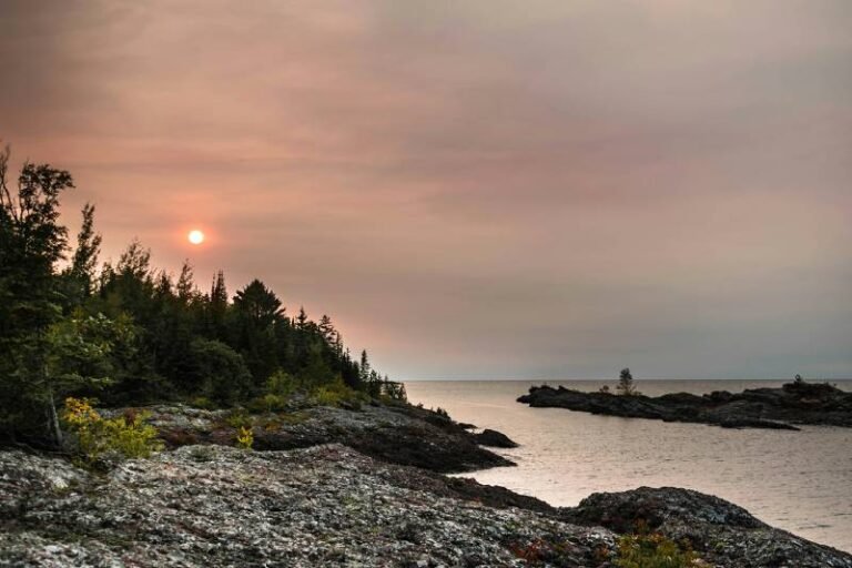 A rocky coastline with the sun setting behind a hill.