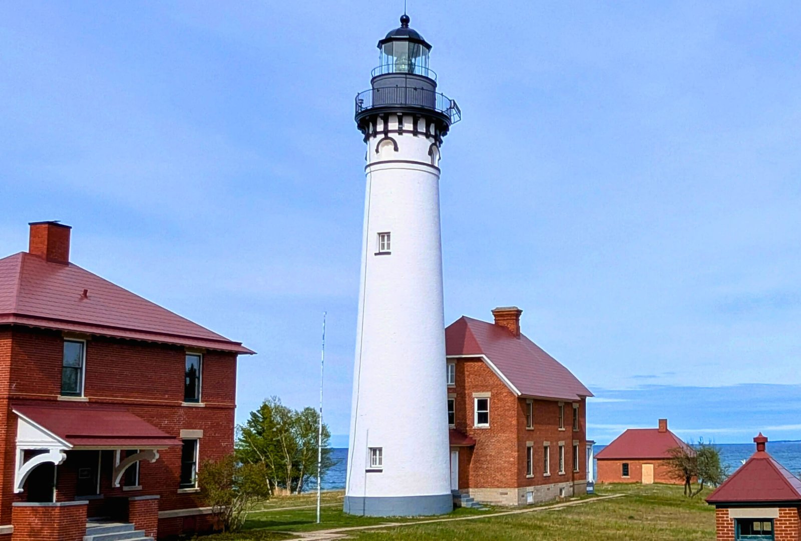 Au Sable Light Station, a large white conical tower with a black cap and attached dwelling surrounded by red brick aux buildings.