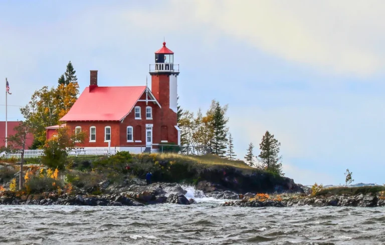 Eagle Harbor Lighthouse, a red brick dwelling attached to a white light tower on a rocky lake shore.