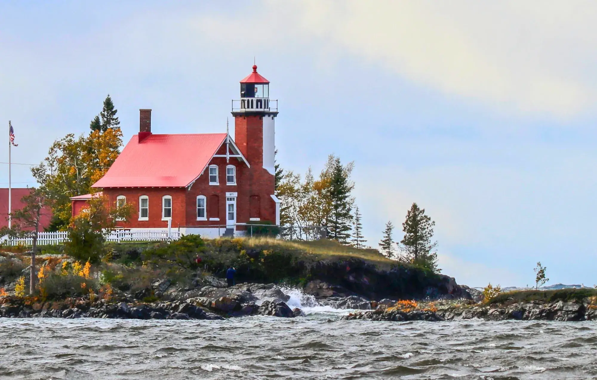 Eagle Harbor Lighthouse, a red brick dwelling attached to a white light tower on a rocky lake shore.