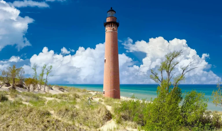 Little Sable Point Lighthouse, a red brick tower flanked by sand dunes and blue water.