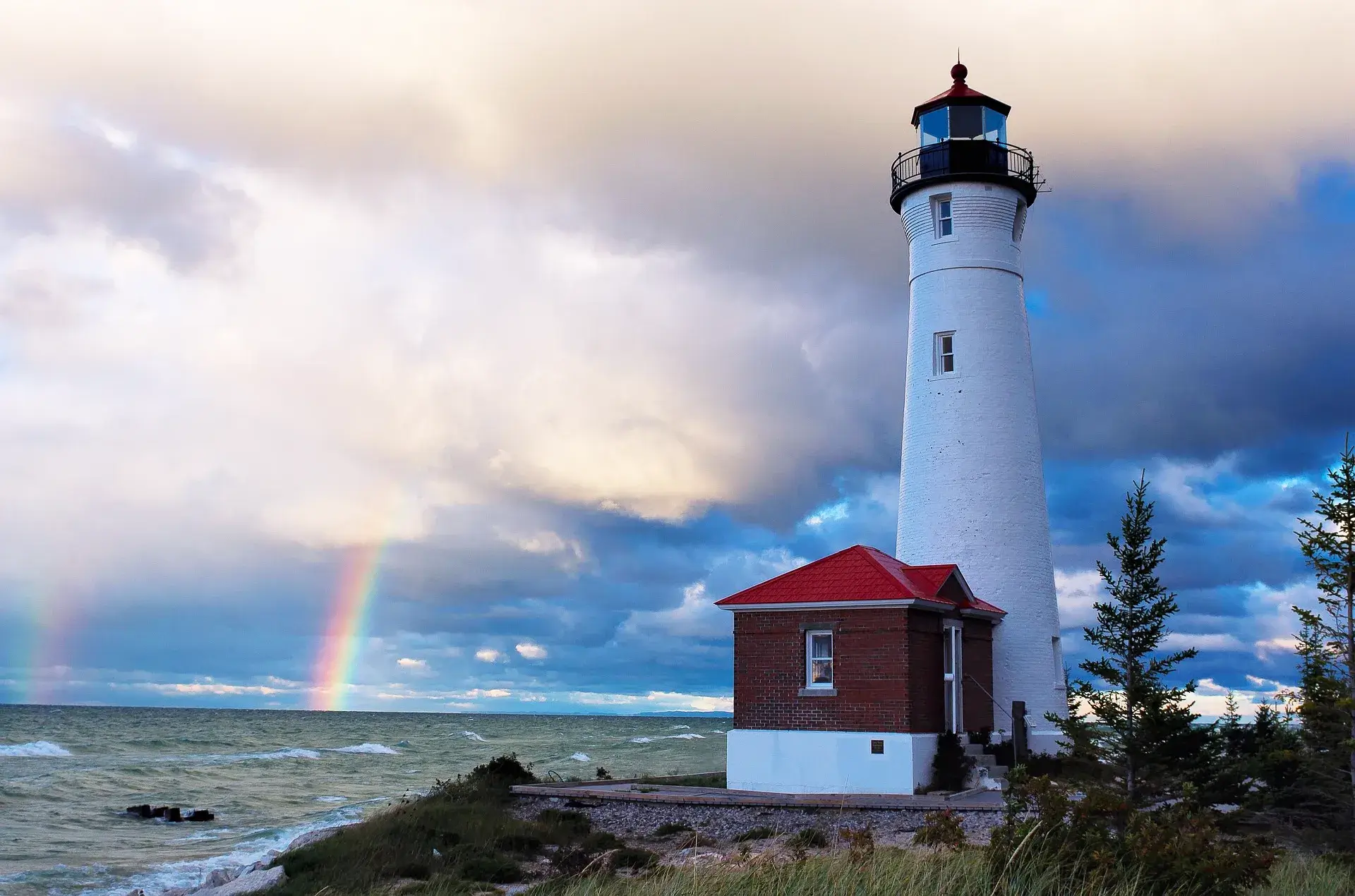 Crisp Point Lighthouse, a large white conical tower on a short rocky cliff with a small attached keeper's dwelling.